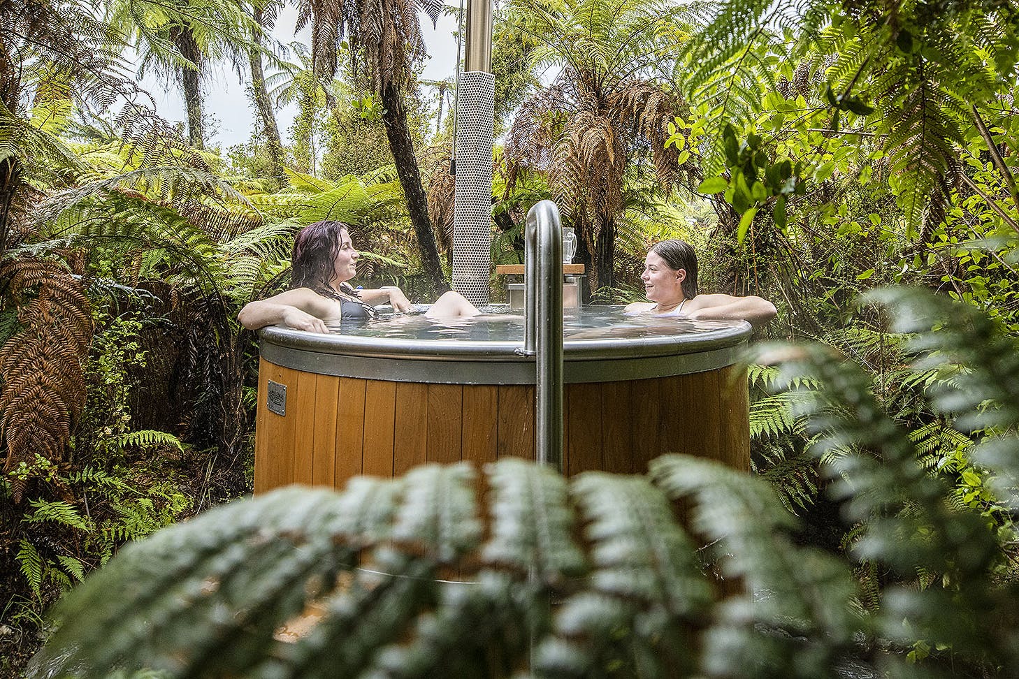 Two people soak in a hot tub amongst greenery.